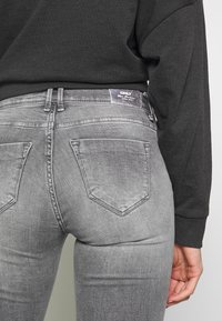 Jeans de denim gris ajustados con un diseño clásico de cinco bolsillos, que presentan un sutil efecto de lavado y una etiqueta trasera con el nombre de la marca.