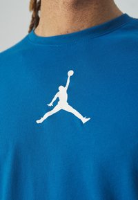 Blå bomullen T-shirt med en stor vit Air Jordan-logotyp. T-shirten har en standard rund halsringning och korta ärmar.