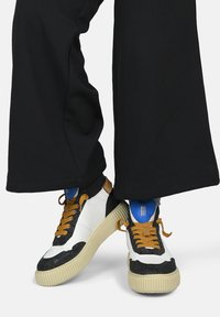 High-top sneakers with white leather and black glitter accents, beige rubber sole, brown laces, and a blue interior.