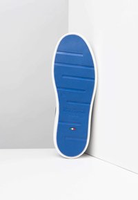 Semelle de sneaker en caoutchouc bleu avec un motif de grip texturé, bord blanc et marque. Présente un petit détail de drapeau italien près du talon.