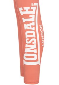 Persikofärgade leggings med en slät yta som har stora vita tryck av "TONSDALE" och "LONDON" på utsidan.