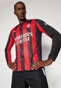 Langærmet fodboldtrøje i rød og sort med lodrette striber, der har "Emirates Fly Better" logoet og et rundt klubmærke.