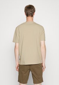 Béžové bavlněné tričko s kulatým výstřihem a krátkými rukávy, doplněné hnědými šortkami. Jednoduchý design, jednobarevné a ležérní střih.