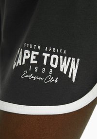 Svarta bomullsshorts med vit kant, prydda med en grafisk utskrift som inkluderar "CAPE TOWN", "1992" och "Exclusive Club" i varierande typsnitt.