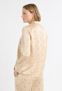 Beżowy zestaw piżamowy o miękkiej fakturze, z zabawnym wzorem zwierząt i kolorowymi akcentami. Wykończony klasycznym kołnierzykiem i mankietami.