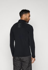 Fekete, hosszú ujjú póló magas gallérral és finom EA7 logóval a hátsó részén. Texturált anyagból készült, testhez álló fazonú. Szürke nadrággal párosítva.