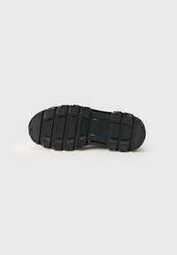 Suela de zapato de goma negra con patrón de agarre texturizado, que presenta secciones elevadas y ranuras para tracción. Bordes suaves y punta redondeada.