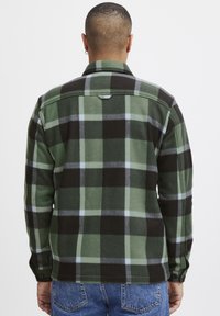 Groen en zwarte geruite fleece shirt met zichtbare stiksels, knoopmanchetten en een kraag. Heeft een ophanglus aan de achterkant.