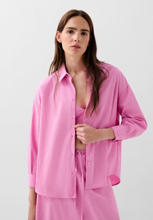 Pink striped blouse with subtle embellishments, featuring a button-down design and long sleeves, paired with a matching pink top and pants.