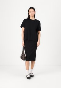 Ensemble comprenant un t-shirt noir court et une jupe mi-longue, en tissu coton doux, assorti à des chaussettes blanches et des chaussures plates noires, et un petit sac.