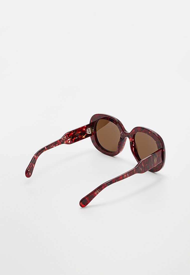 Rote Schildpatt-Sonnenbrille mit braunen Gläsern. Gerundetes Rahmen-Design, dicke Bügel und strukturierte Oberflächendetails. Hardware-Akzent in der Nähe der Scharniere.