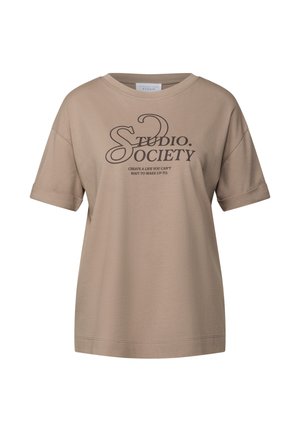 T-shirt oversize beige en coton doux. Présente des manches courtes et un texte imprimé qui dit "STUDIO. SOCIETY" avec un slogan en dessous.