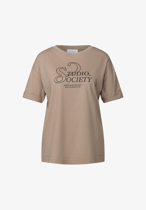 T-shirt oversize beige en coton doux. Présente des manches courtes et un texte imprimé qui dit "STUDIO. SOCIETY" avec un slogan en dessous.