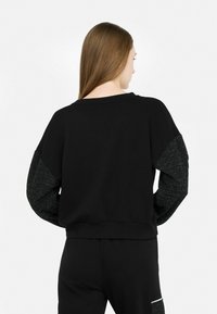 Zwarte sweatshirt met een relaxte pasvorm, brede halslijn en een textuur met sprankelende zwarte accenten op de mouwen. Glad materiaal overal.