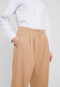 Jasnoniebieska i biała koszula w paski z zapięciem na guziki, w połączeniu z beżowymi spodniami z wysokim stanem i plisami, posiadającymi boczne kieszenie.