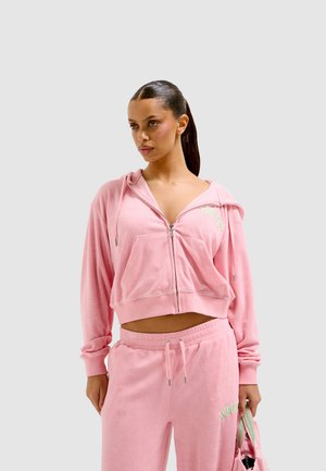 Pink velour zip-up hoodie with front pocket and green "JUICY" text, paired with matching sweatpants featuring a drawstring waist.