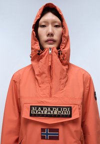 Oranje ritjack met capuchon, flapzak aan de voorkant en patches met een logo en de vlag van Noorwegen. Gemaakt van lichtgewicht, gestructureerde stof.