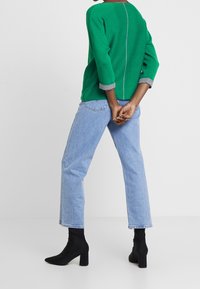Groene trui met grijze mouwen, gecombineerd met lichtblauwe rechttoe-rechtaan jeans en zwarte blokhak enkellaarsjes. Eenvoudig ontwerp en een ontspannen pasvorm.