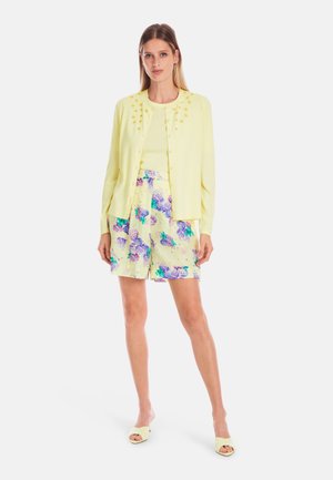 Light yellow cardigan with floral embellishments, worn over a matching top and pastel shorts featuring a floral print in purple and green.