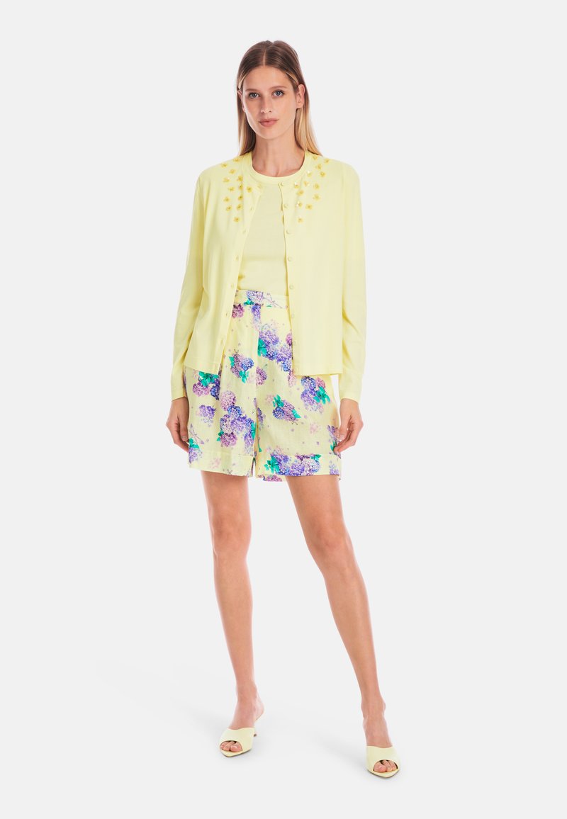 Light yellow cardigan with floral embellishments, worn over a matching top and pastel shorts featuring a floral print in purple and green.