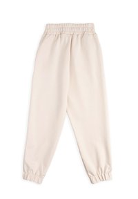 Kremowe dresy wykonane z miękkiego materiału. Posiadają elastyczny pas i zwężane mankiety przy kostkach. Brak widocznych wzorów lub elementów metalowych.