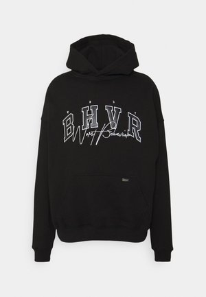 Black hooded sweatshirt with front kangaroo pocket, featuring white outlined letters "BHV R" and cursive "Worst Behavior" text across the chest.