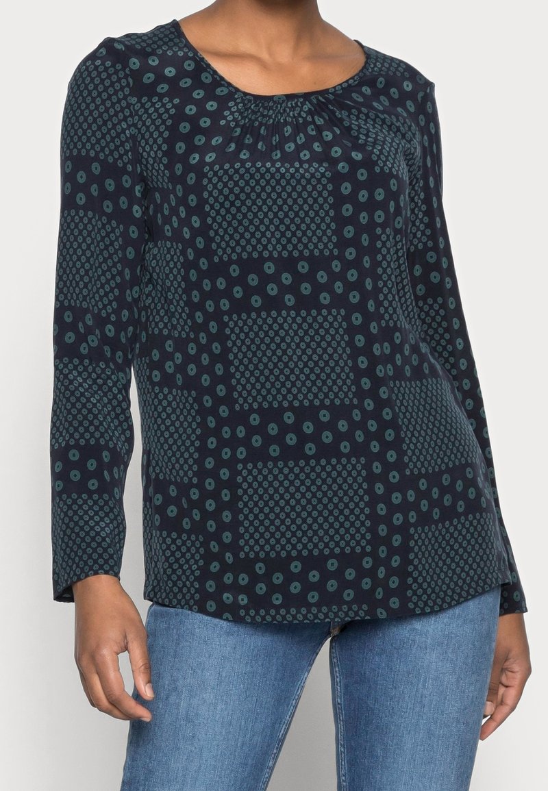 Top bleu marine à manches longues avec des motifs circulaires et carrés en vert bleuâtre. Caractérisé par un col froncé et un tissu doux et léger.