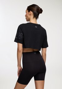 T-shirt nera cropped con maniche corte che presenta la scritta "I'm" sul retro e pantaloni corti neri a vita alta. Design semplice e aderente.