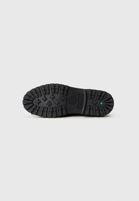 Suola di sneakers in gomma nera con scanalature profonde e motivi incrociati. Presenta un'impronta del logo e un piccolo accento blu vicino al centro.