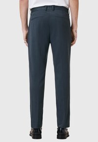 Ciemnoszare spodnie o prostym kroju, z paskami do paska, dwoma tylnymi kieszeniami i gładką fakturą materiału. Noszone z czarnymi butami.