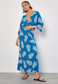 Completo due pezzi blu composto da un top corto con nodo frontale e motivi bianchi a forma di foglia, abbinato a una gonna lunga, entrambi realizzati in un tessuto leggero.