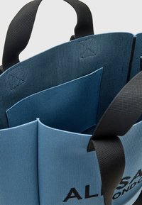 Niebieska torba na ramię z fakturowanym wykończeniem, czarnymi uchwytami oraz przestronnym wnętrzem z dodatkową kieszenią. Czarny nadrukowany logo na boku.
