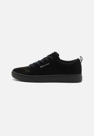 Zapatilla de ante negra con un diseño suave, suela de goma, cordones planos y un acento de logo en el lateral. Textura suave y perfil bajo.