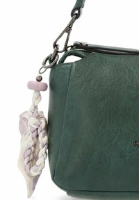 Angolo di borsa in pelle verde scuro con un portachiavi intrecciato in bianco e lavanda attaccato a un gancio metallico sulla tracolla.