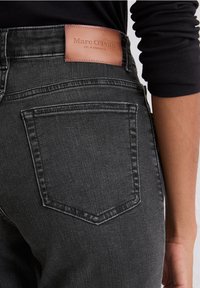 Jean gris foncé en denim, avec une texture lisse, un design à cinq poches et une étiquette en cuir marron portant "Marc O'Polo" sur la taille.
