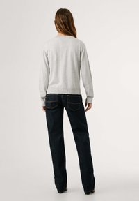 Maglione grigio a collo rotondo con maniche lunghe abbinato a jeans dritti blu scuro. Il maglione presenta polsini e orlo a coste; i jeans hanno tasche posteriori.