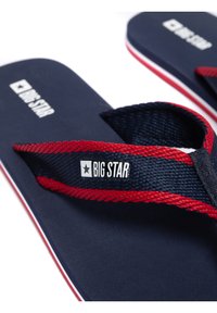 Modré žabky s červenými akcenty a popruhy, s texturovaným designem a štítkem s logem na popruhu. Ikonický bílý okraj kolem podešve.