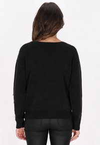 Pullover negru din tricot, cu o croială lejeră, tiv striat și mâneci lungi. Textură moale, fără modele sau accesorii vizibile.