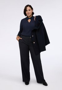 Blusa navy con cuello decorado y detalle de ojal, combinada con pantalones de pierna ancha en gris oscuro. Incluye un abrigo navy colgado de un brazo.