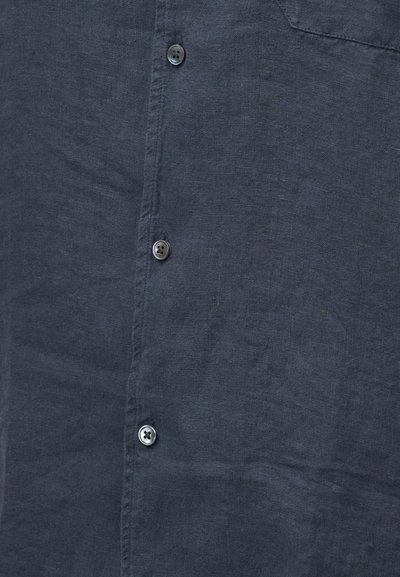 Σκούρο μπλε λινό πουκάμισο εμπρός με τρία ορατά κουμπιά και διακριτή υφή υφάσματος.