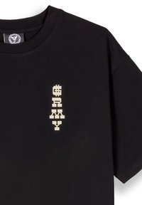 Camiseta de algodón negra con un gráfico vertical en letras mayúsculas y en negrita de color blanco que dice "ARMY", con formas de letras y acentos distintivos.