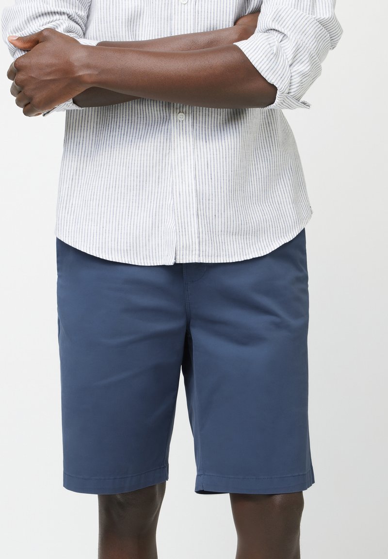 Shorts azul marino hechos de una tela ligera, con una textura suave y un corte hasta la rodilla, combinados con una camisa blanca de botones con rayas.