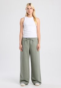 White ribbed tank top paired with high-waisted, wide-leg, light green striped pants featuring an elastic waistband and side pockets.
