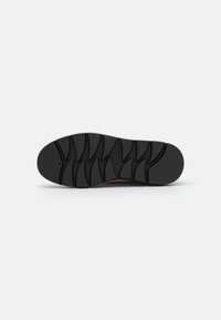 Black rubber shoe sole with deep tread pattern, featuring curved grooves and a smooth toe area, designed for traction and support.