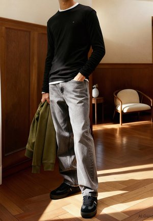 Schwarzes Langarmshirt mit weißem Halsausschnitt, graue Jeans, schwarze Sneakers und eine olivgrüne Kapuzenjacke in der Hand. Hintergrund aus Holzvertäfelung und Parkettboden.