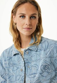 Jasnoniebieska kurtka dżinsowa z białym haftem kwiatowym, zapięcie na zatrzaski z przodu oraz detal w kołnierzu. Posiada teksturowany materiał i swobodny krój.