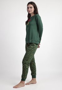 Top verde de manga larga con un gráfico de paraguas rojo y pantalones verdes con un patrón de pequeñas flores amarillas, fabricados en una tela suave.