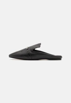 Mula de cuero negra con punta afilada, tipo slip-on, con un tacón bajo y plano y una correa decorativa sobre la parte superior.