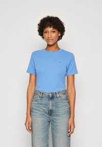 Kortermet blå bomull T-skjorte med rund hals, med et lite logo på brystet, kombinert med høyt liv lyse denim jeans.
