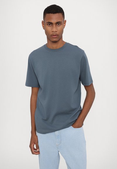 Blå bomulds T-shirt med korte ærmer og rund halsudskæring, parret med lyse denim jeans, der har en afslappet pasform og glat tekstur.